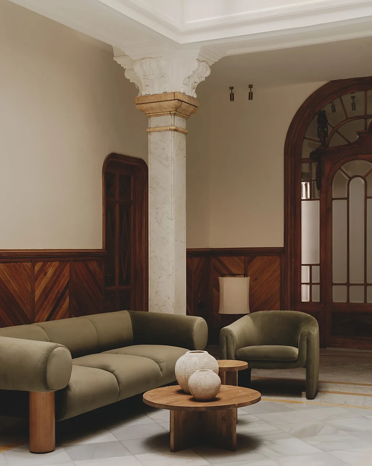 Salon de Casa Llimona avec canapé et fauteuil verts, au pied d'une colonne en marbre
