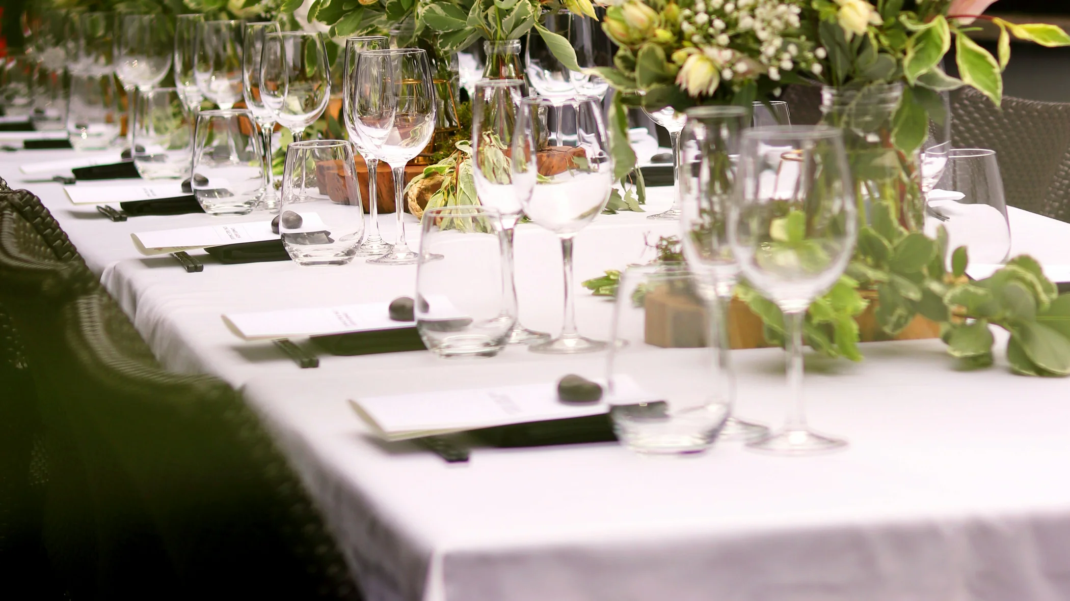 Table de réception dressée au jardin, avec fleurs, verres et guirlandes lumineuses