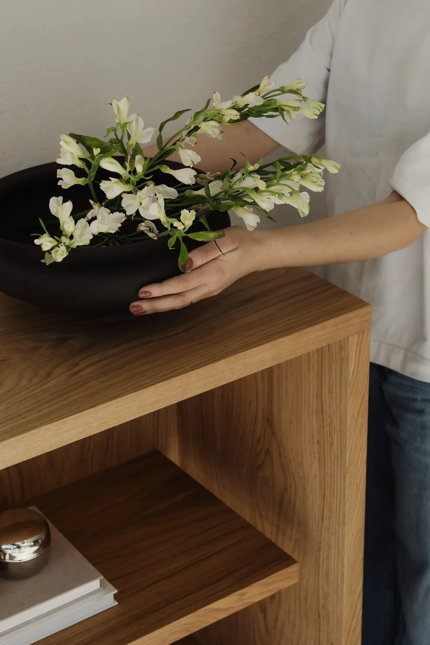Mains posant un bol noir garni de fleurs blanches sur un meuble en bois