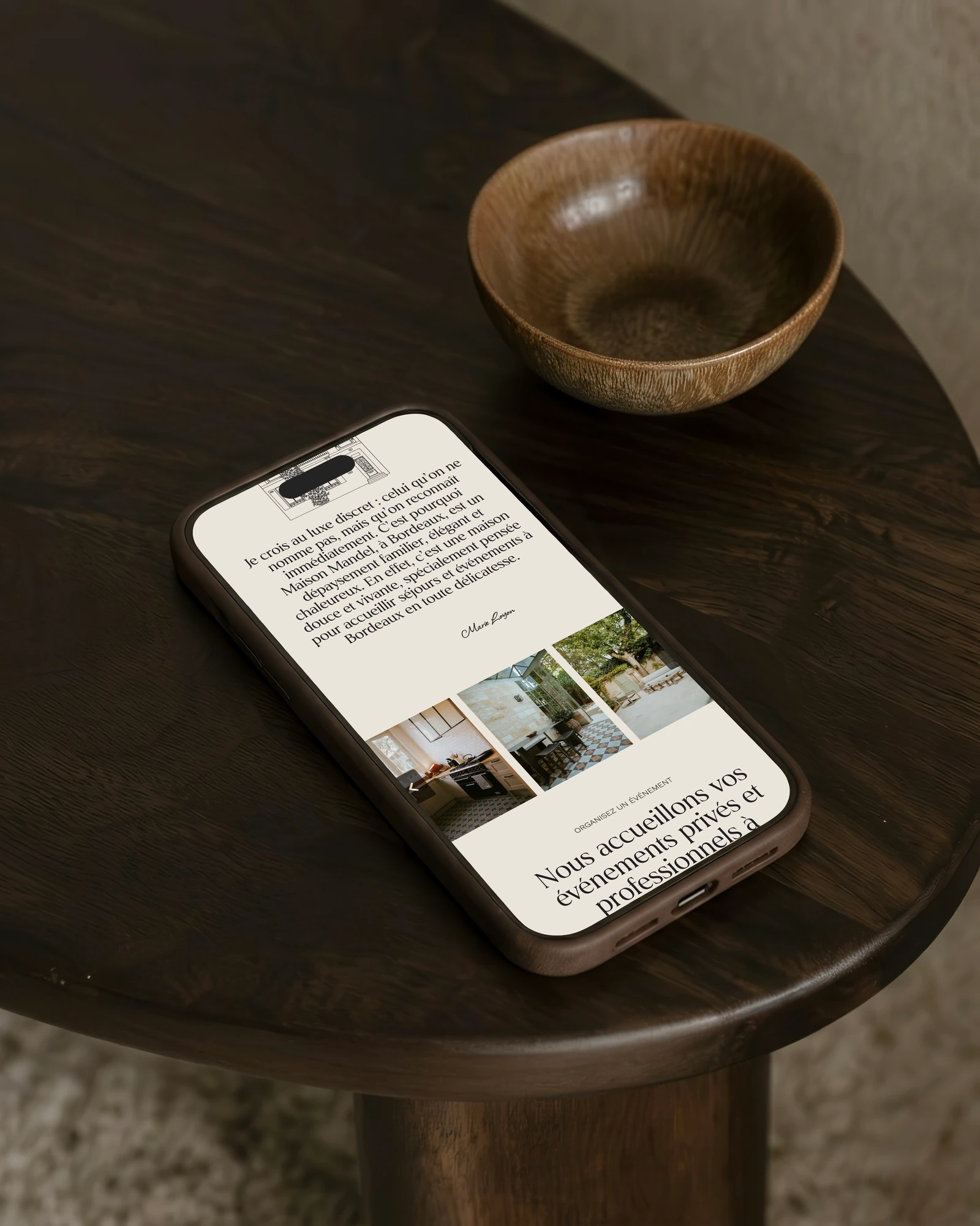 Page d'accueil de Maison Mandel sur un téléphone posé sur une table ronde en bois sombre