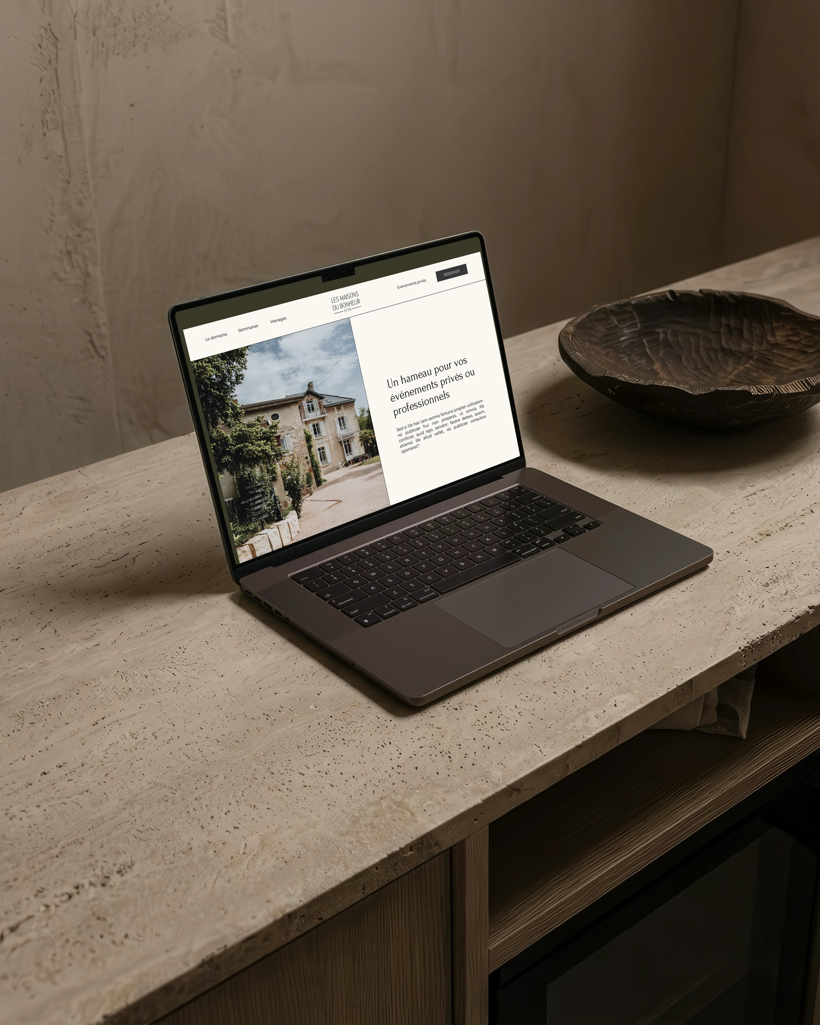 Page d'accueil du concept des Maisons du Bonheur sur un ordinateur portable posé sur un plan en travertin