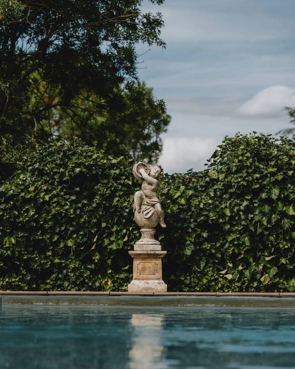 La piscine du domaine et sa statue, devant une haie de verdure