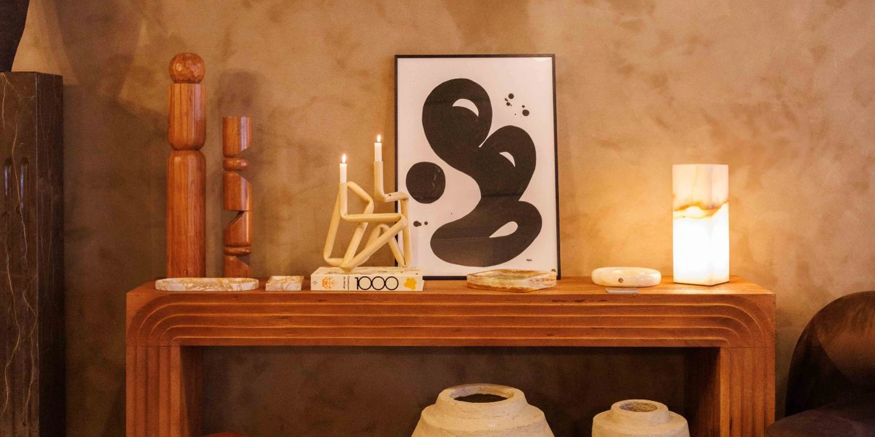 Une console en bois sculpté avec bougeoir, œuvre graphique, lampe en onyx et vases, sous des luminaires en papier mâché