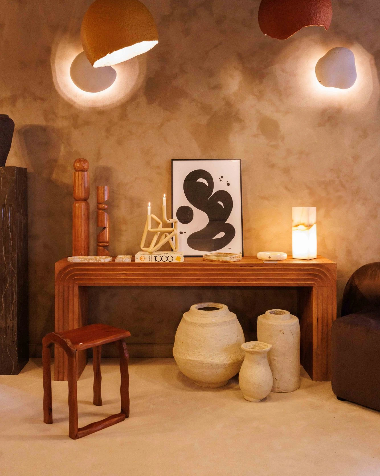 Une console en bois sculpté avec objets décoratifs, vases en terre et tabouret, sous deux luminaires