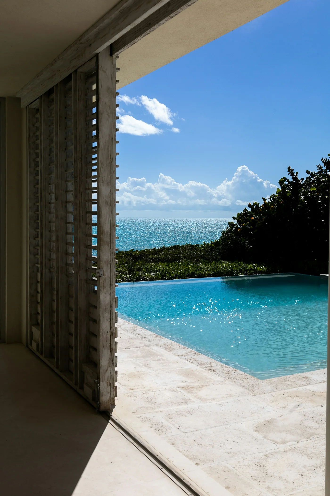 Piscine à débordement avec vue sur la mer, vue depuis une pièce aux persiennes